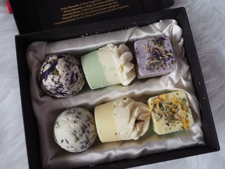 Geöffnete schwarze Geschenkbox mit goldener Prägung, sechs Satin Naturel Badepralinen auf edlem Satinstoff gebettet, bereit für ein luxuriöses Spa-Erlebnis zu Hause.