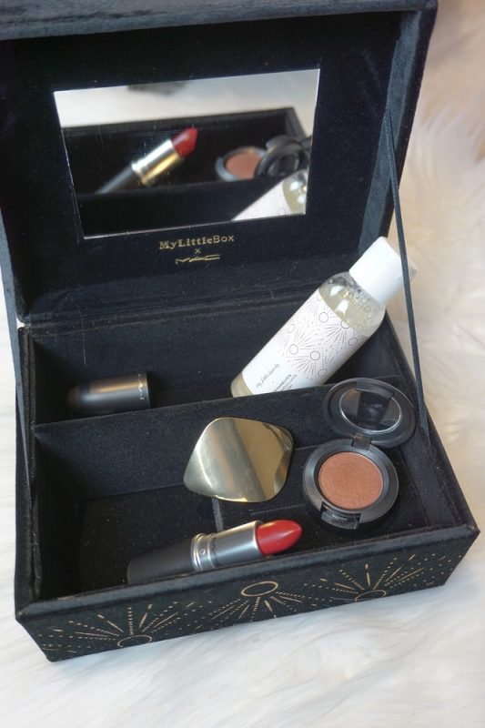 Hochkantaufnahme der dunkelblauen Samtschatulle der My Little Box mit MAC-Produkten auf weißem Fell – Lidschatten, Lippenstift und Pflegeprodukte elegant arrangiert.